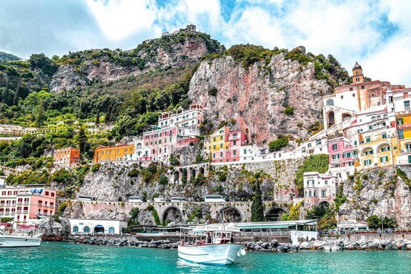 Une ville côtière aux bâtiments aux couleurs vives, avec une falaise rocheuse et un bateau sur l’eau. 1
