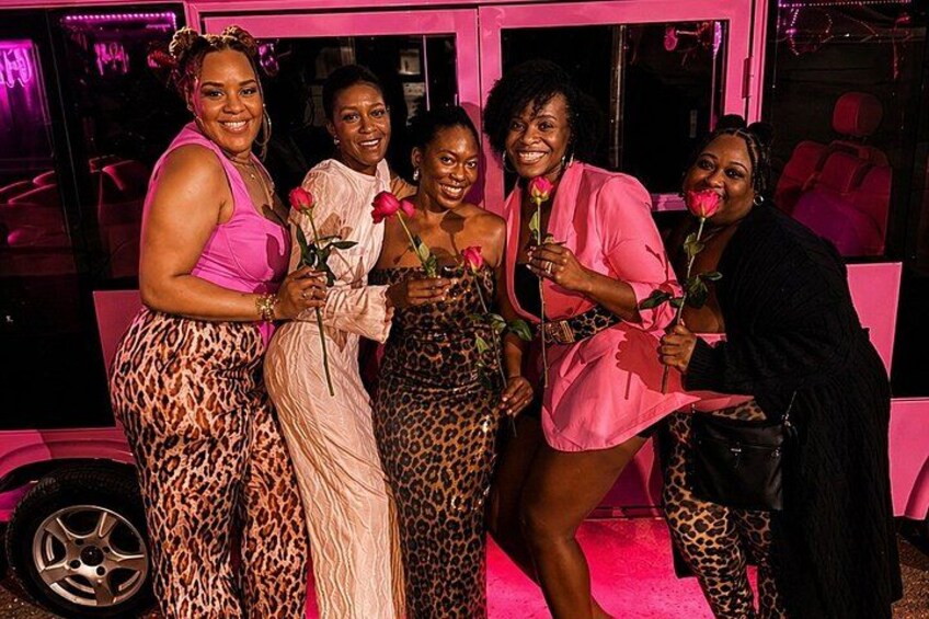 A group of people posing in front of a pink vehicle with leopard print patterns. 4