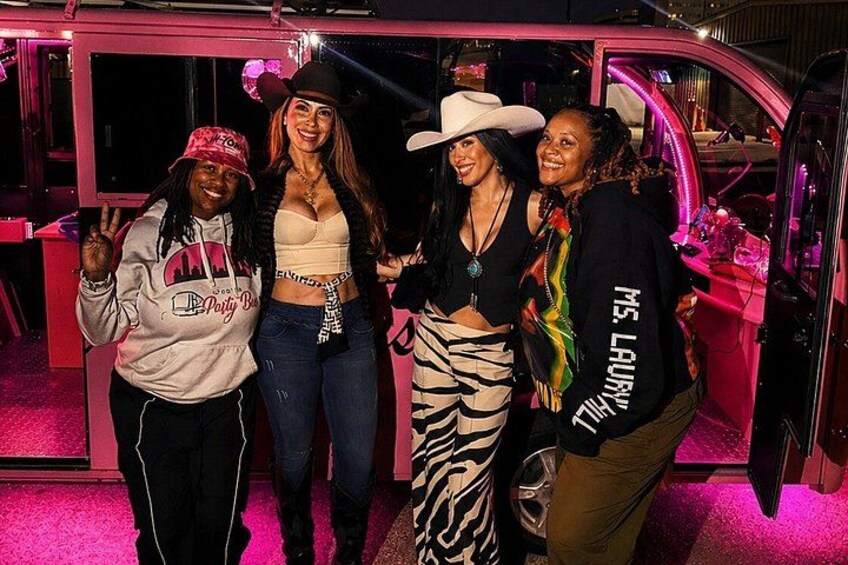 A group of people posing in a pink-lit indoor setting with a vehicle in the background. 3