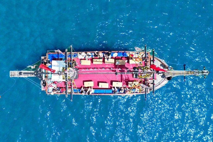 An aerial view of a large, colorful floating platform with multiple levels and structures, surrounded by blue water. 3