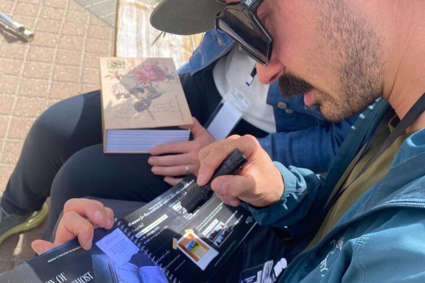 Una persona seduta all'aperto, che tiene un libro e uno smartphone. 3