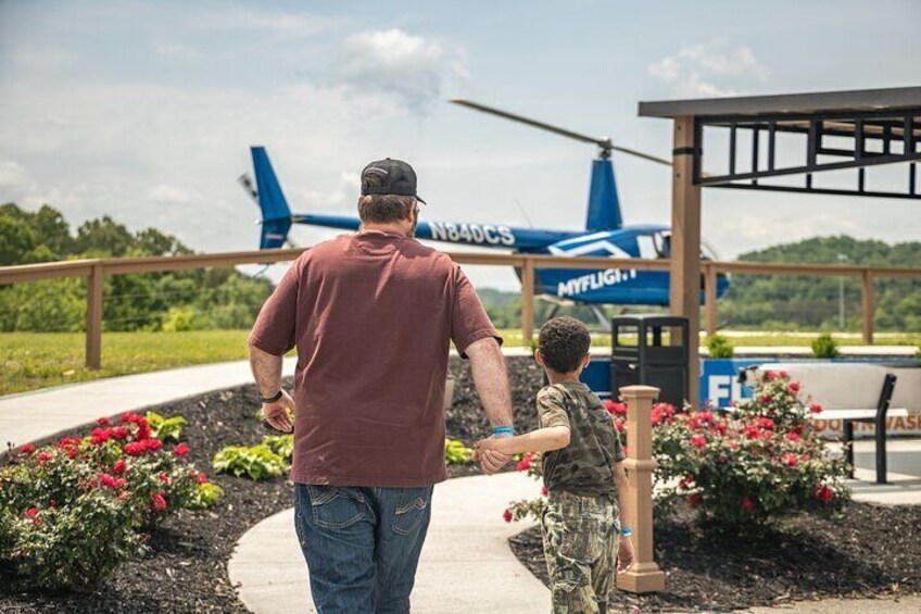 A man and a child walking on a path with a blue helicopter in the background. 5