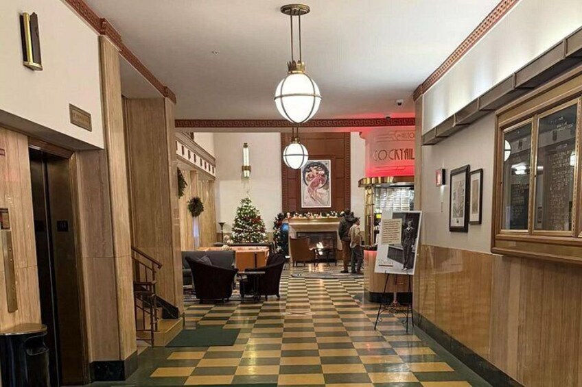 A hotel lobby with a checkered floor, a Christmas tree, a bar area, and a staircase. 2