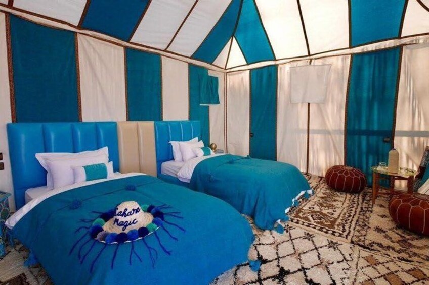 A tented accommodation with two beds, blue bedding, and a patterned rug. 1
