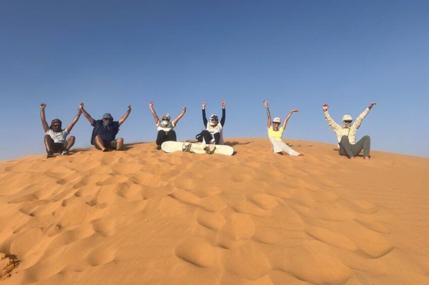 A group of people sitting on a sand dune with their arms raised. 4