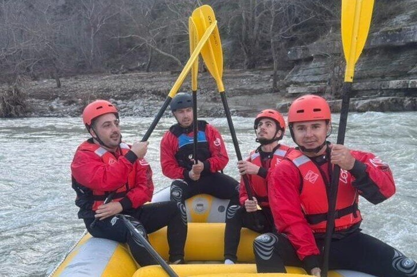 Three people in a yellow inflatable raft with paddles, wearing red jackets and helmets, on a river. 1