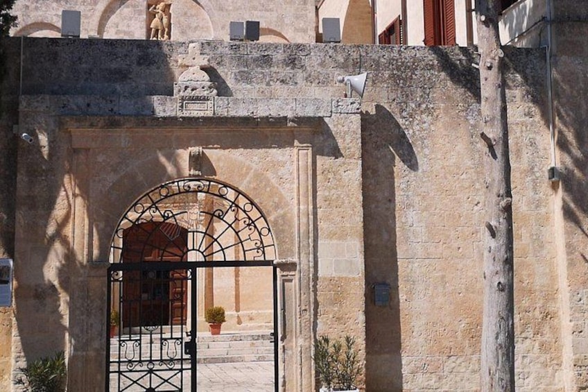 A stone gate with an arched entrance, a potted plant, and a statue on top of a wall. 2