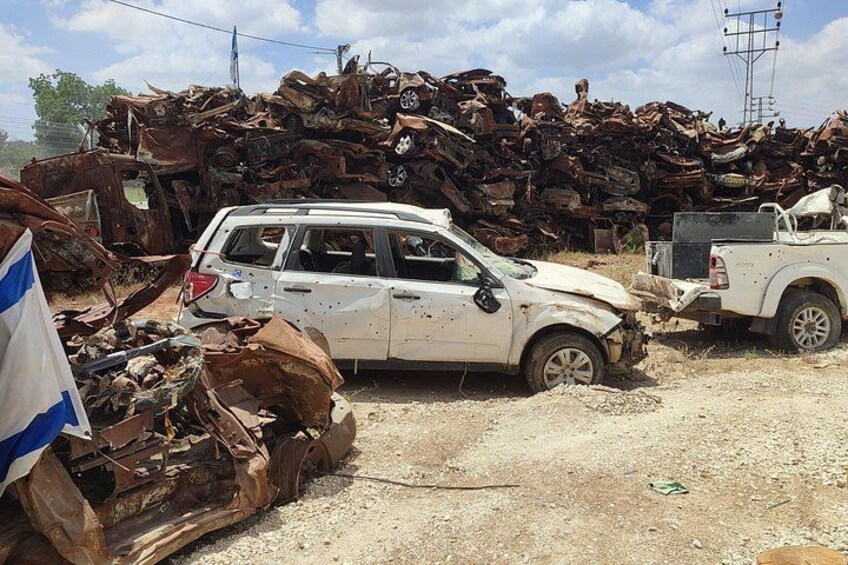 A white SUV parked in a junkyard with a large pile of rusted metal debris in the background. 2