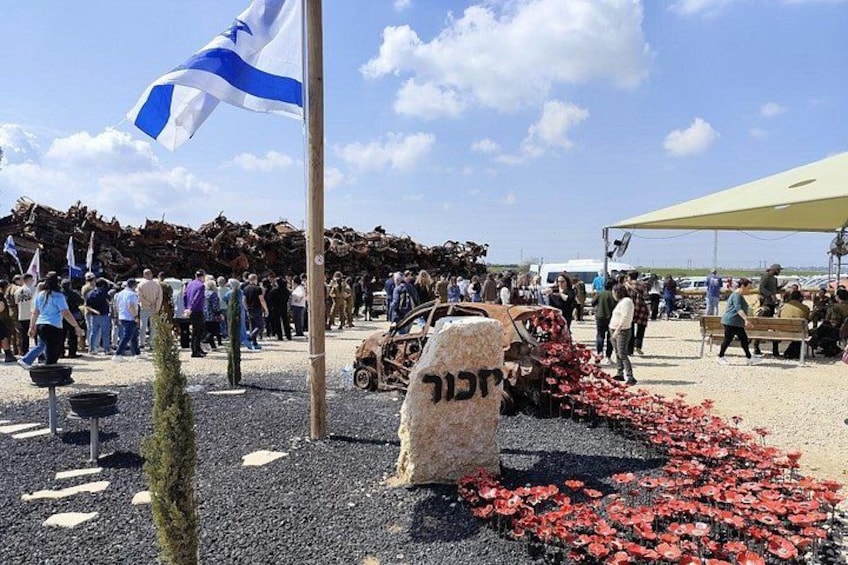 A public gathering with a flag, a stone monument, and a pathway. 1