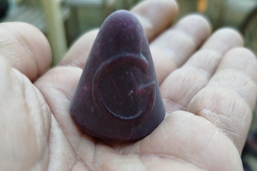 A hand holding a dark purple, cone-shaped object with a circular indentation. 2
