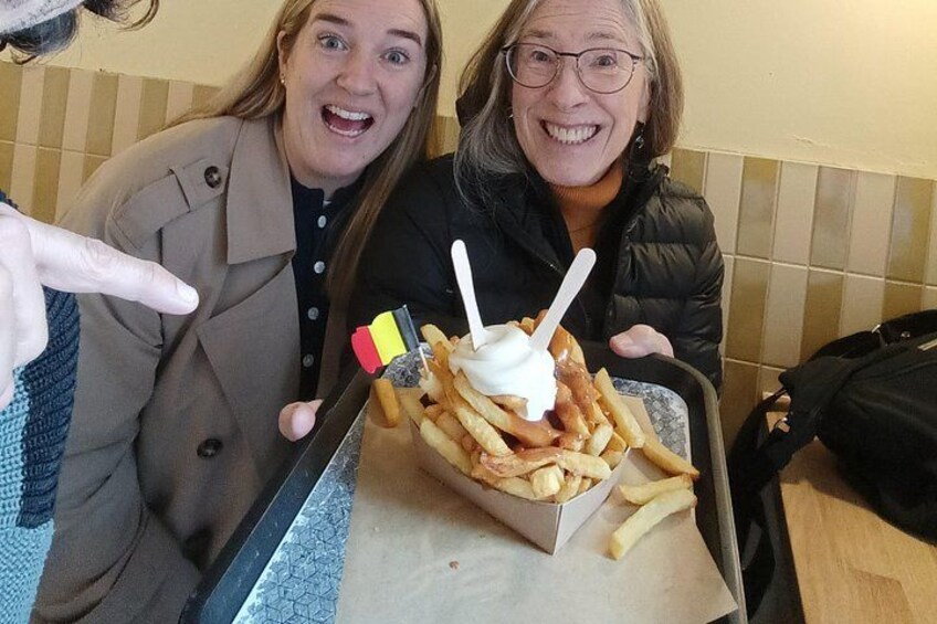Two people sitting at a table with a tray of fries and a white cup with a straw. 1