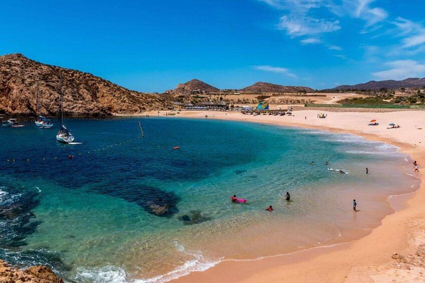 A beach with clear turquoise water, a sandy shore, and a rocky hill in the background. 5