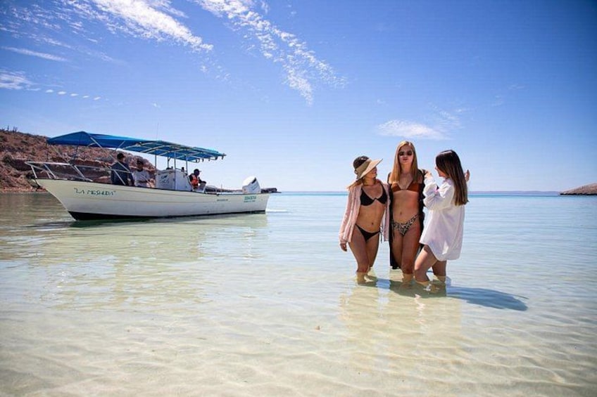 A boat named 'LA FERRO' on calm waters, people walking in shallow water, and a clear sky. 1