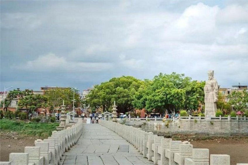 A pathway leading to a statue, surrounded by trees and a fence. 3