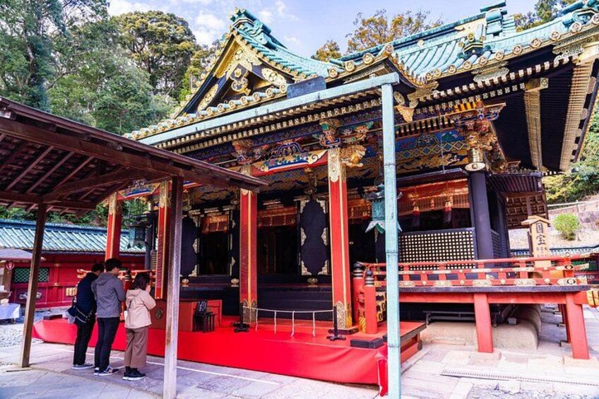 A traditional Japanese temple with a red and gold roof, a wooden structure in front, and people standing in front. 3
