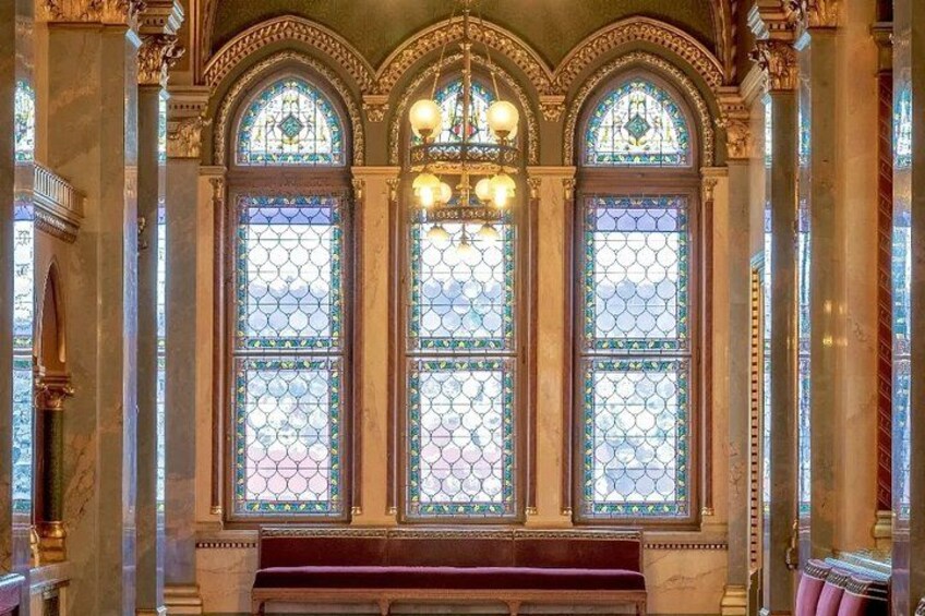 Una imponente ventana de vitral con diseños complejos y un banco debajo. 3