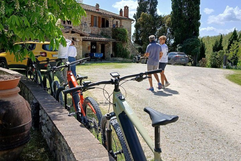 Bicycles parked along a stone wall, a yellow vehicle, and two people walking in a courtyard. 3