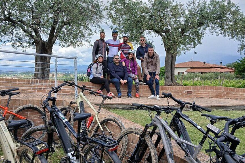 A group of people posing with bicycles in a park with trees and a view of the landscape. 2