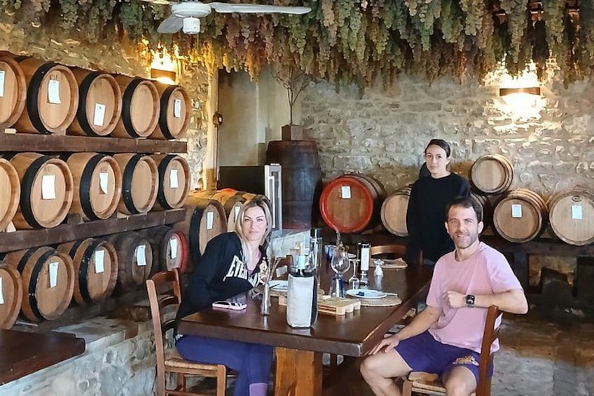 A wine cellar with wooden barrels, a table with wine glasses, and a person standing. 5