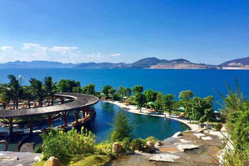 Piscina de un resort con muelle de madera, rodeada de palmeras y rocas. 2