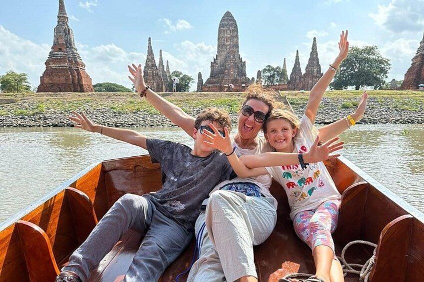A group of people in a wooden boat on a river with ancient temple structures in the background. 1