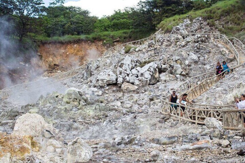 Un paysage volcanique avec une passerelle en bois et des personnes observant l’activité géothermique. 1