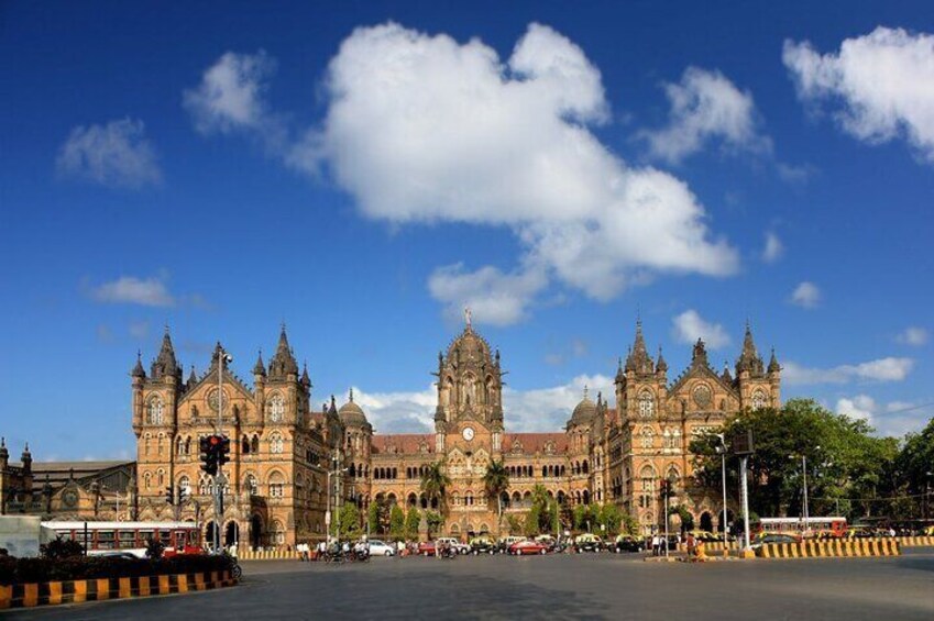 A large, ornate building with multiple towers and a clock tower, surrounded by a busy street and clear blue sky. 3