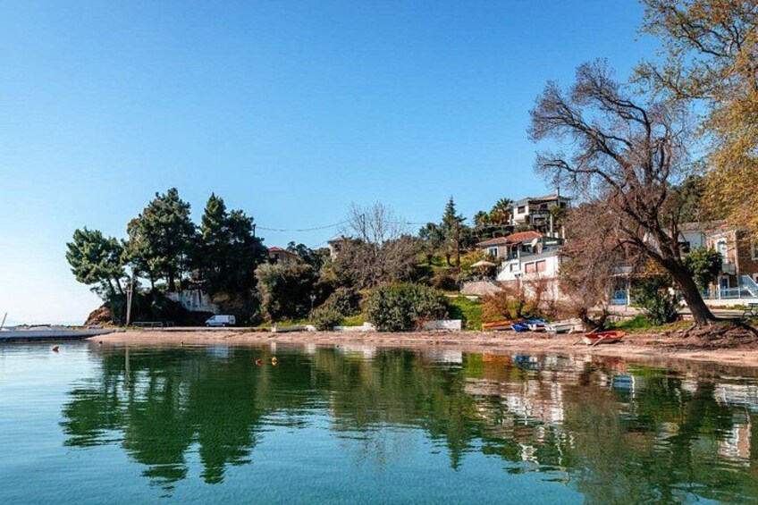 A calm lake with reflections, a shoreline with trees and buildings, and a clear blue sky. 5