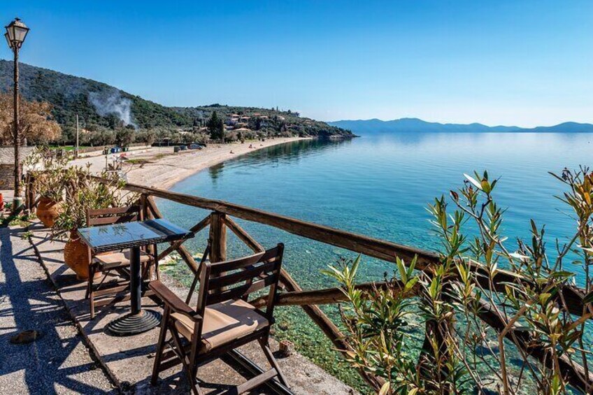 A lakeside terrace with wooden furniture and a view of a beach and mountains. 2