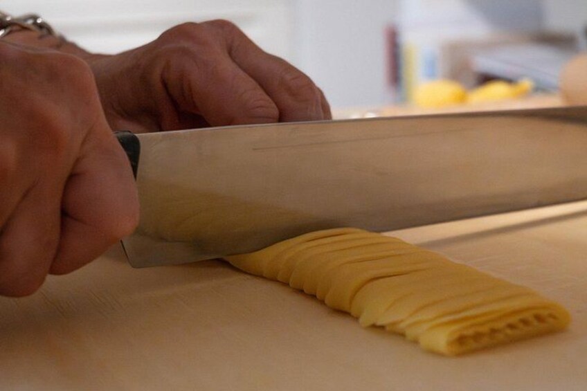 Hands using a large knife to slice a yellow food item on a cutting board. 3