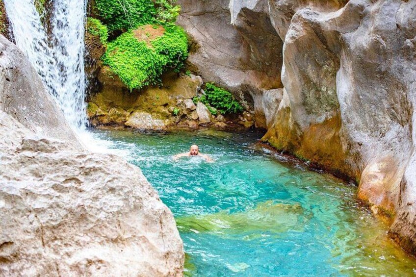 A person swimming in a clear blue pool with a waterfall in the background. 1