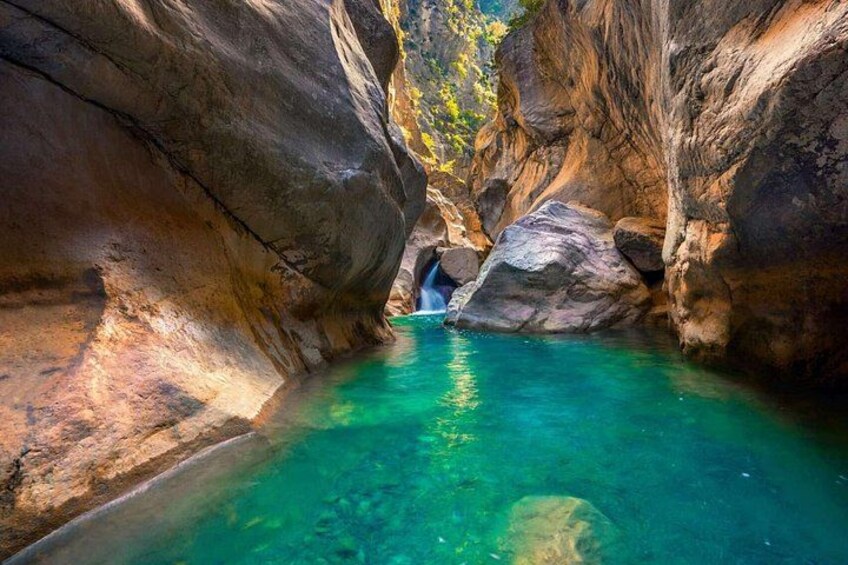 A clear blue pool surrounded by rocky cliffs with a waterfall in the background. 3