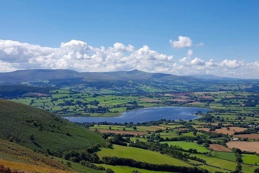 A valley with a lake, rolling hills, and distant mountains under a clear sky. 2