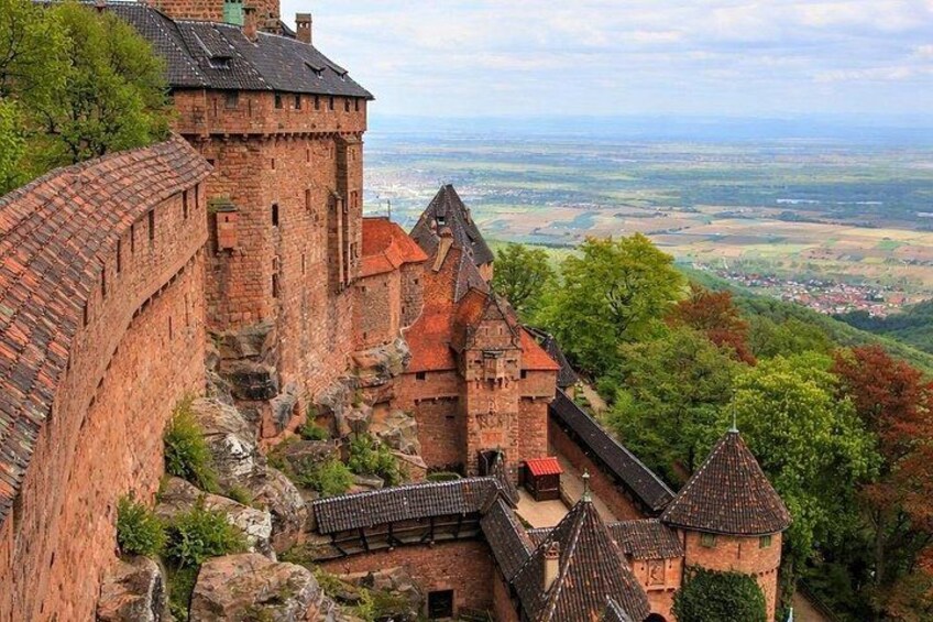 A historic stone castle with a red-tiled roof, surrounded by lush greenery and a panoramic view of the countryside. 3