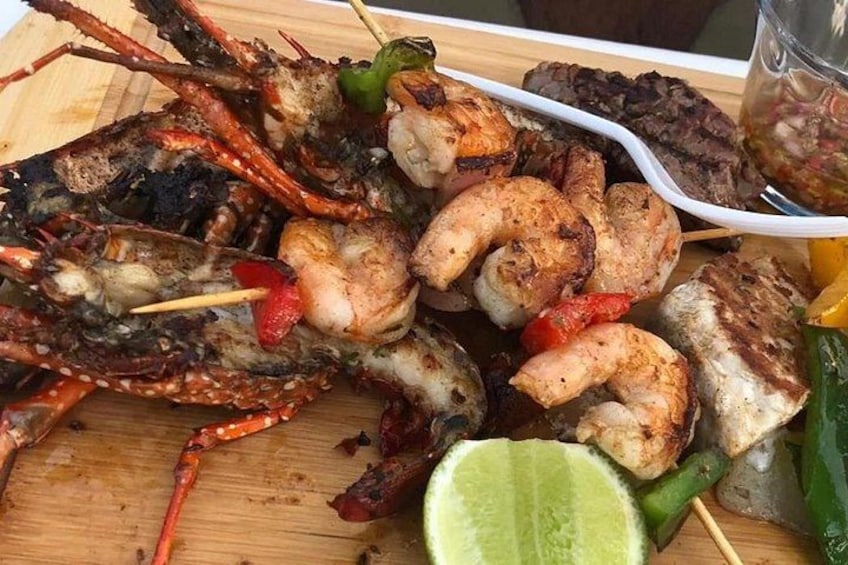 Grillspieße mit gegrilltem Fisch und einer Limettenspalte auf einer Holzbrett. 2