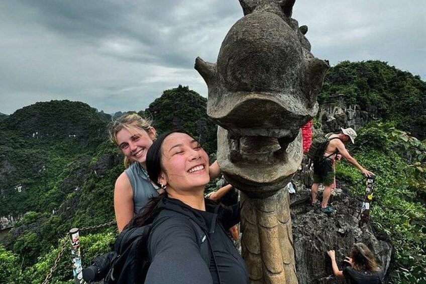 En person tager selfies med en stor stenskulptur i et bjergrigt område. 2