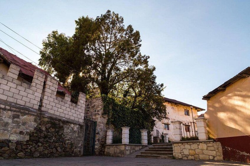 A stone building with a red roof, a tree in front, and a staircase leading up to a door. 3