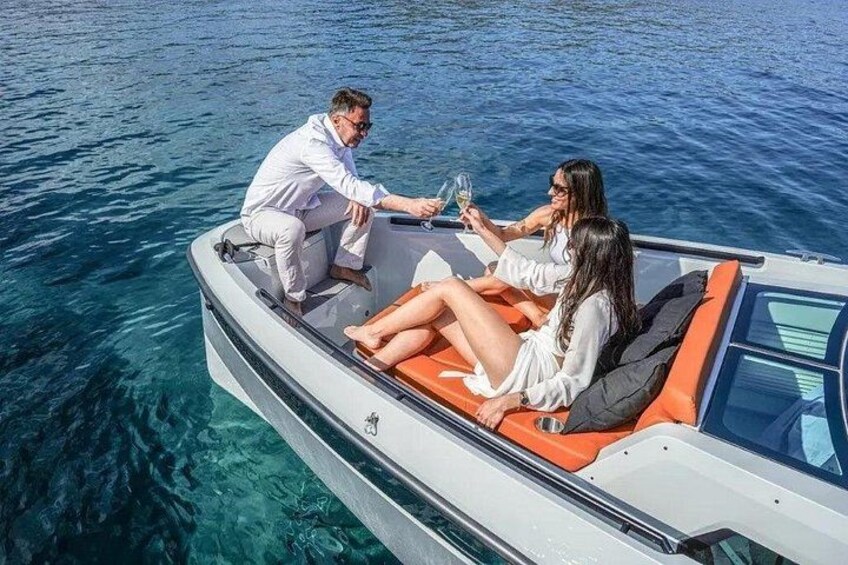 A small motorboat on clear blue water with two people on the deck, one steering and one holding a glass. 4
