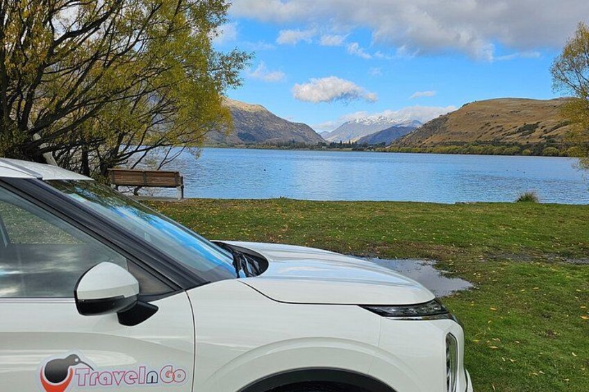 Un coche blanco aparcado junto a un lago con montañas al fondo. 3