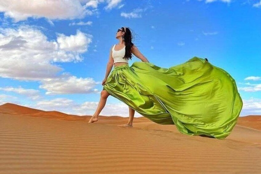 A person in a white top and green skirt walking on a desert with sand dunes and a clear sky. 1