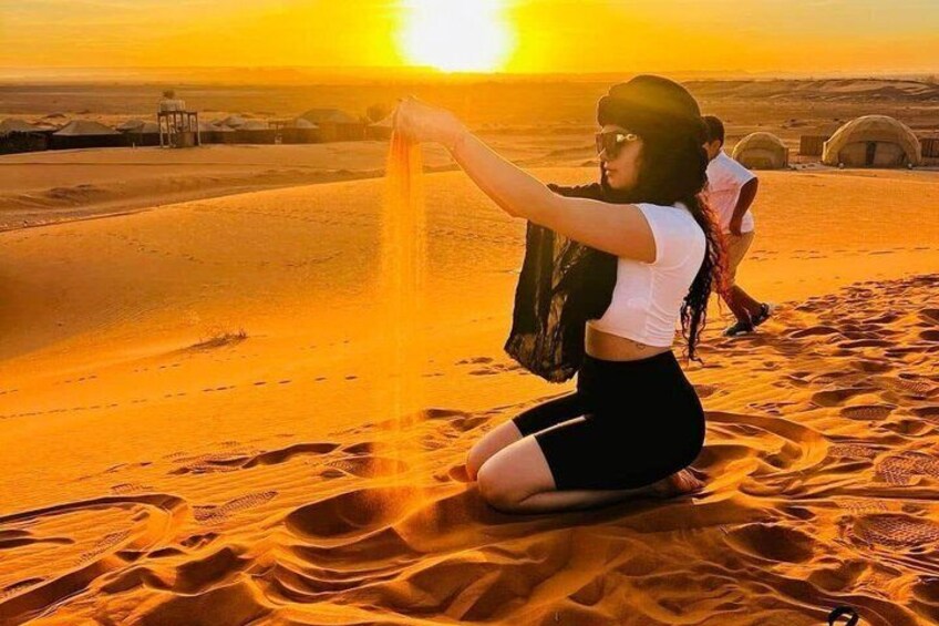 A person sitting on sand dunes at sunset, with another person in the background. 3