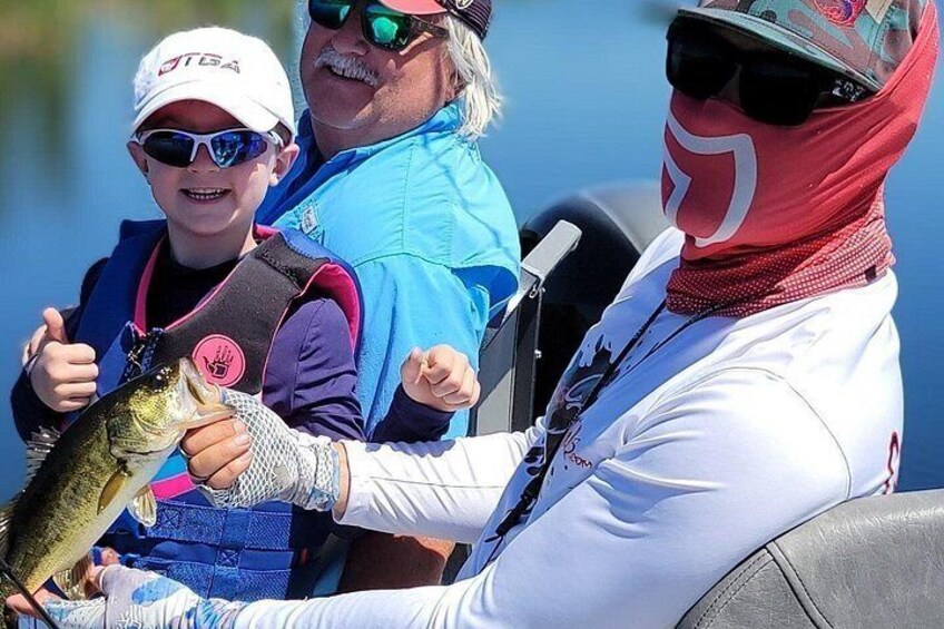 A person holding a fish, wearing a life jacket, and another person in a boat. 1