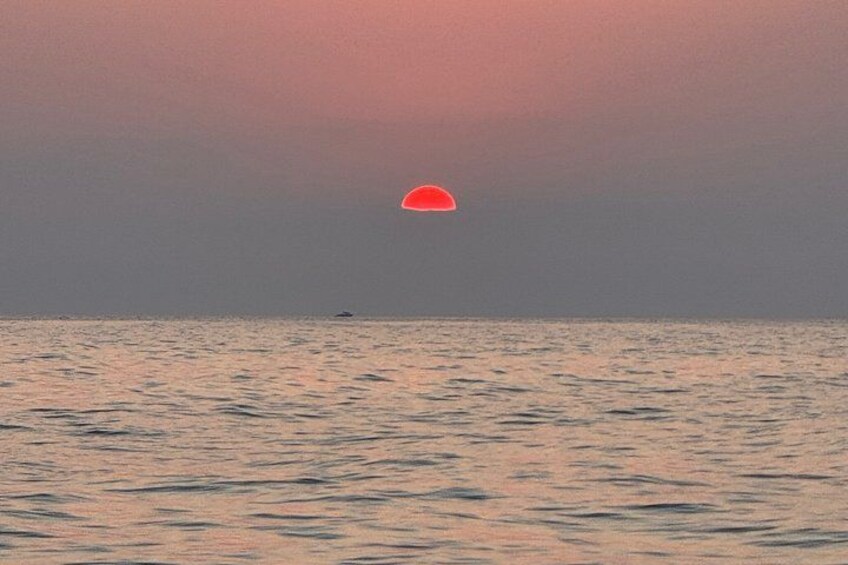 A sunset over a calm sea with a small boat in the distance. 4