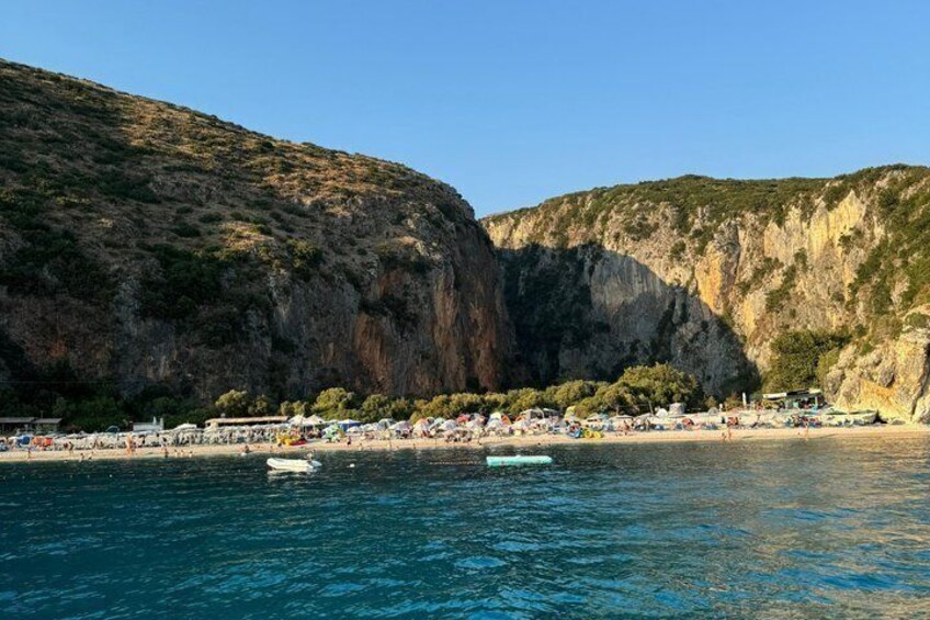 A coastal beach with rocky cliffs, clear blue water, and several boats. 4