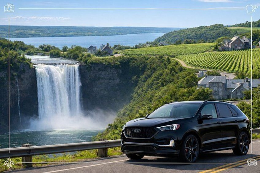 En svart SUV på en väg med ett vattenfall och vingårdar i bakgrunden. 1