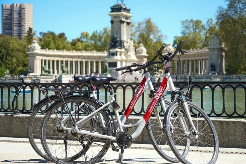 Een fiets met rood en wit frame geparkeerd bij een reling, met een fontein en klassieke architectuur op de achtergrond. 3
