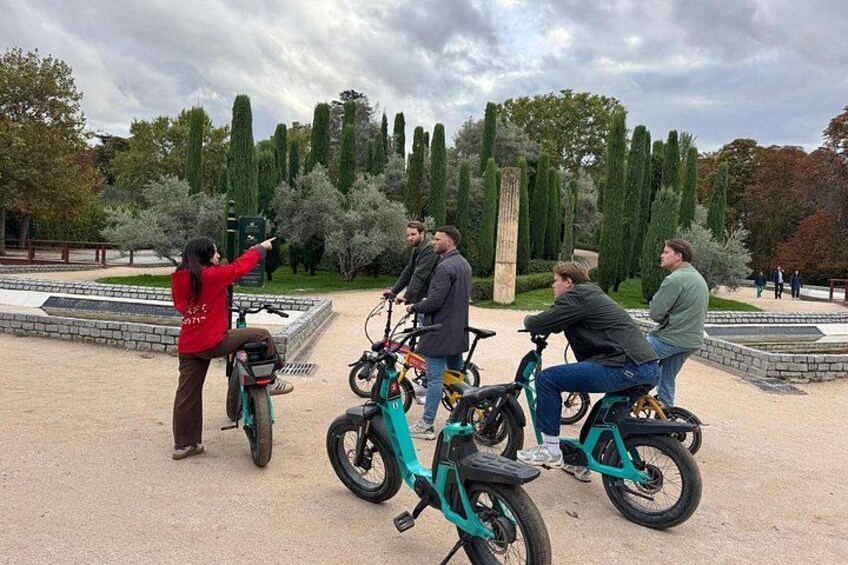 Een groep mensen die op elektrische scooters rijdt in een park met bomen en een fontein. 1