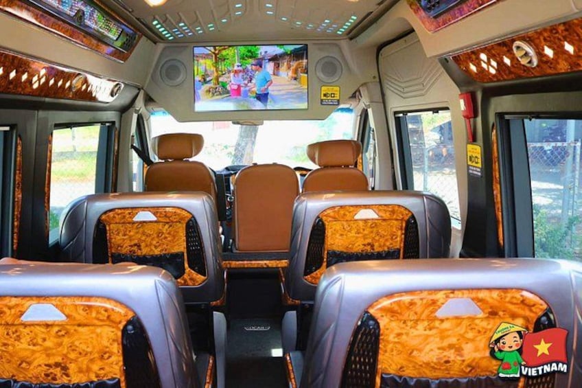 A bus interior with brown leather seats, a central aisle, and a television screen displaying a street scene. 3