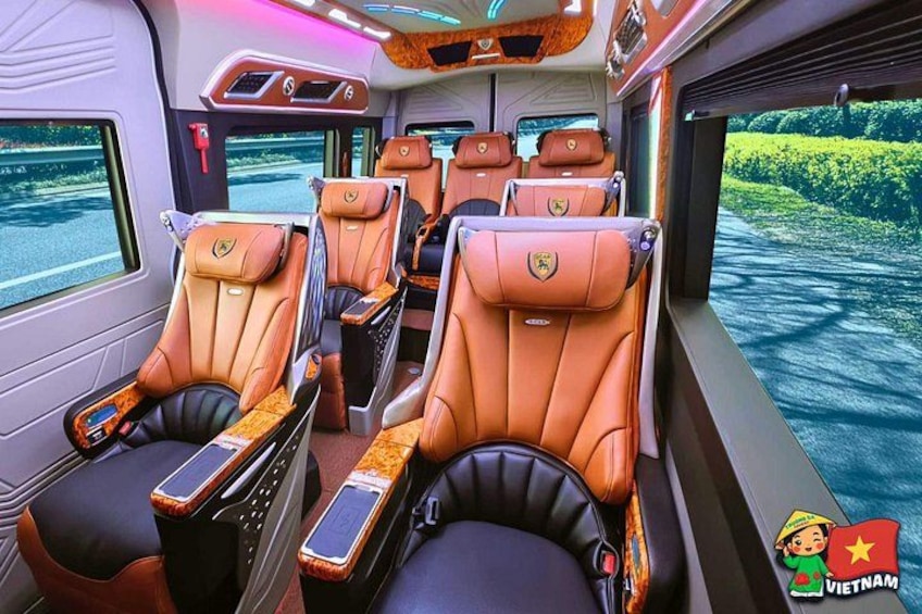 A train interior with leather seats, wooden paneling, and a window view of greenery. 4