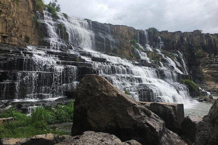 A multi-tiered waterfall cascading over rocky terrain with lush greenery at the base. 1